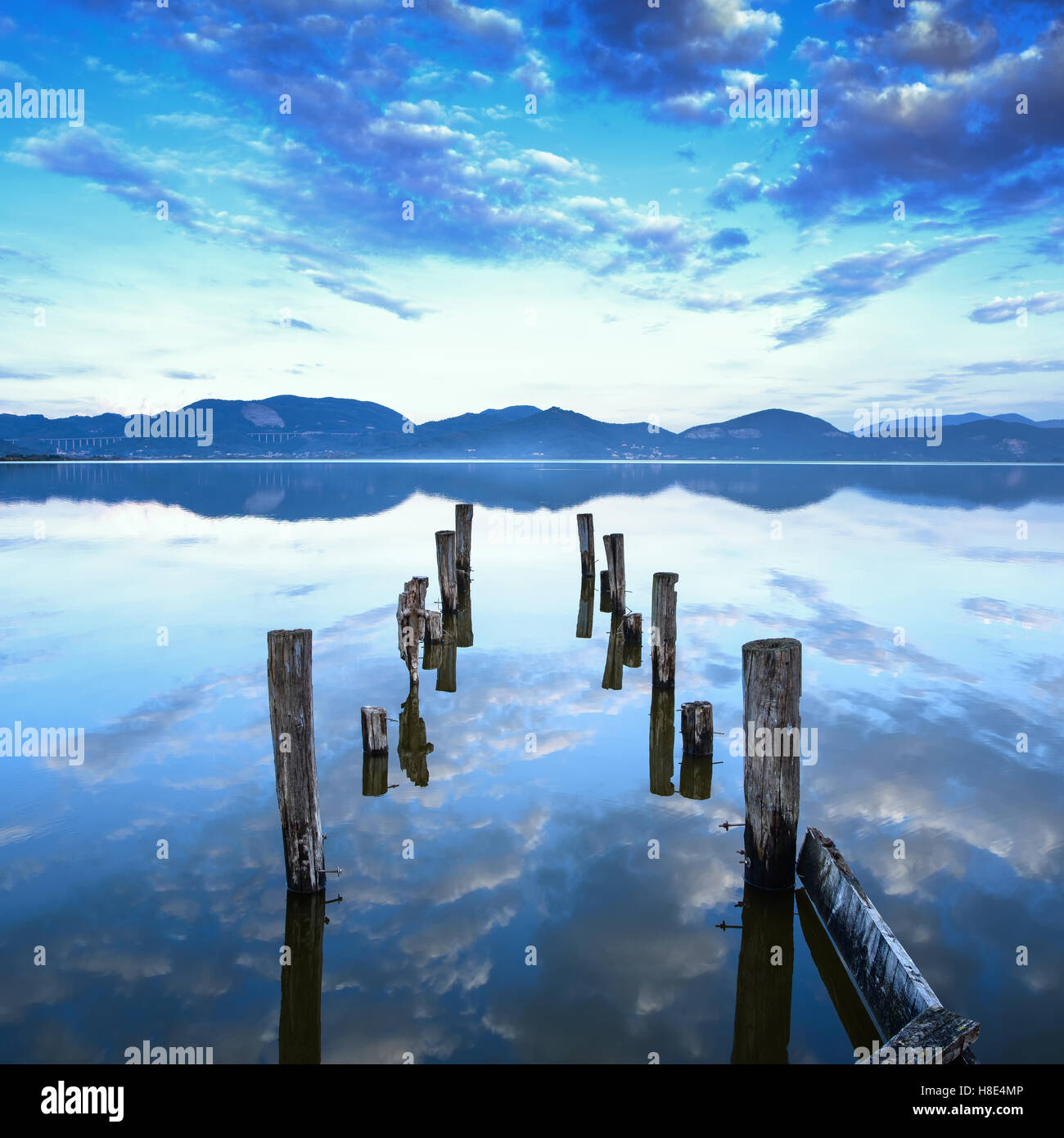 Wooden pier or jetty remains on a blue lake sunset and cloudy sky reflection on water. Versilia Massaciuccoli, Tuscany, Italy. Stock Photo