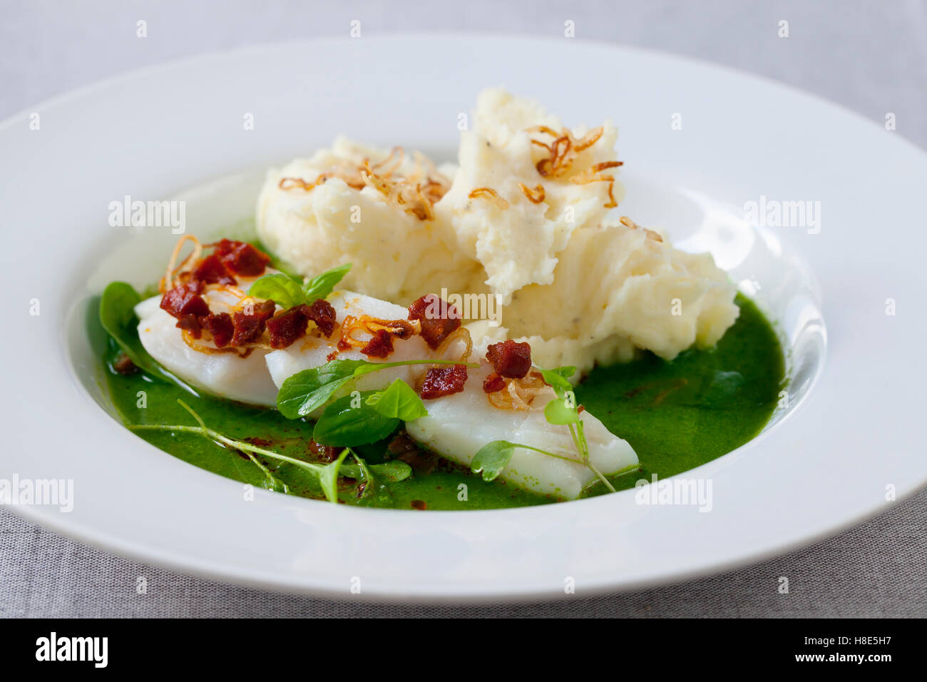 Butter poached cod with green peas, spinach and basil veloute, crispy chorizo and shallots Stock Photo