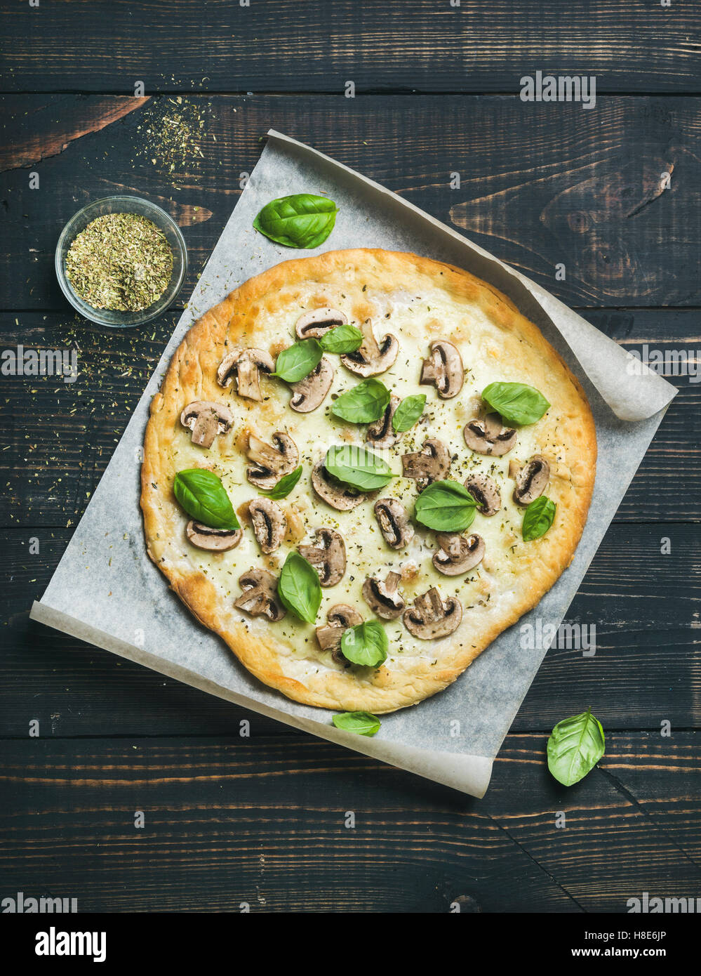 Homemade mushroom pizza with basil leaves and spices in glass on baking paper over dark scorched wooden background, top view, ve Stock Photo