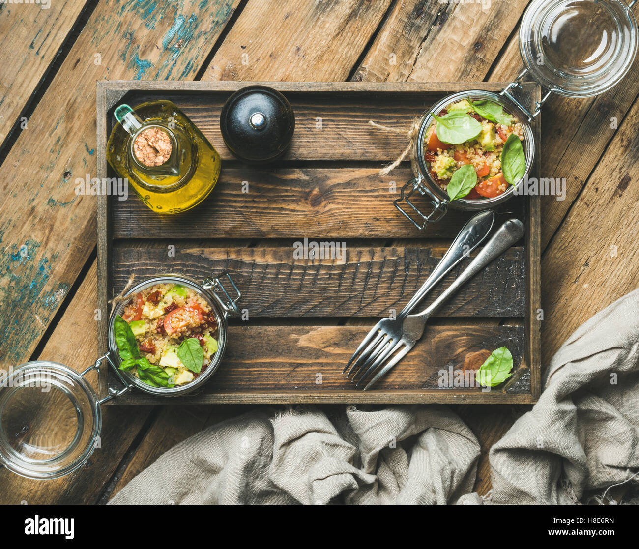 Healthy homemade glass jar quinoa salad with cherry and sun-dried tomatoes, avocado, basil in wooden box over rustic background, Stock Photo