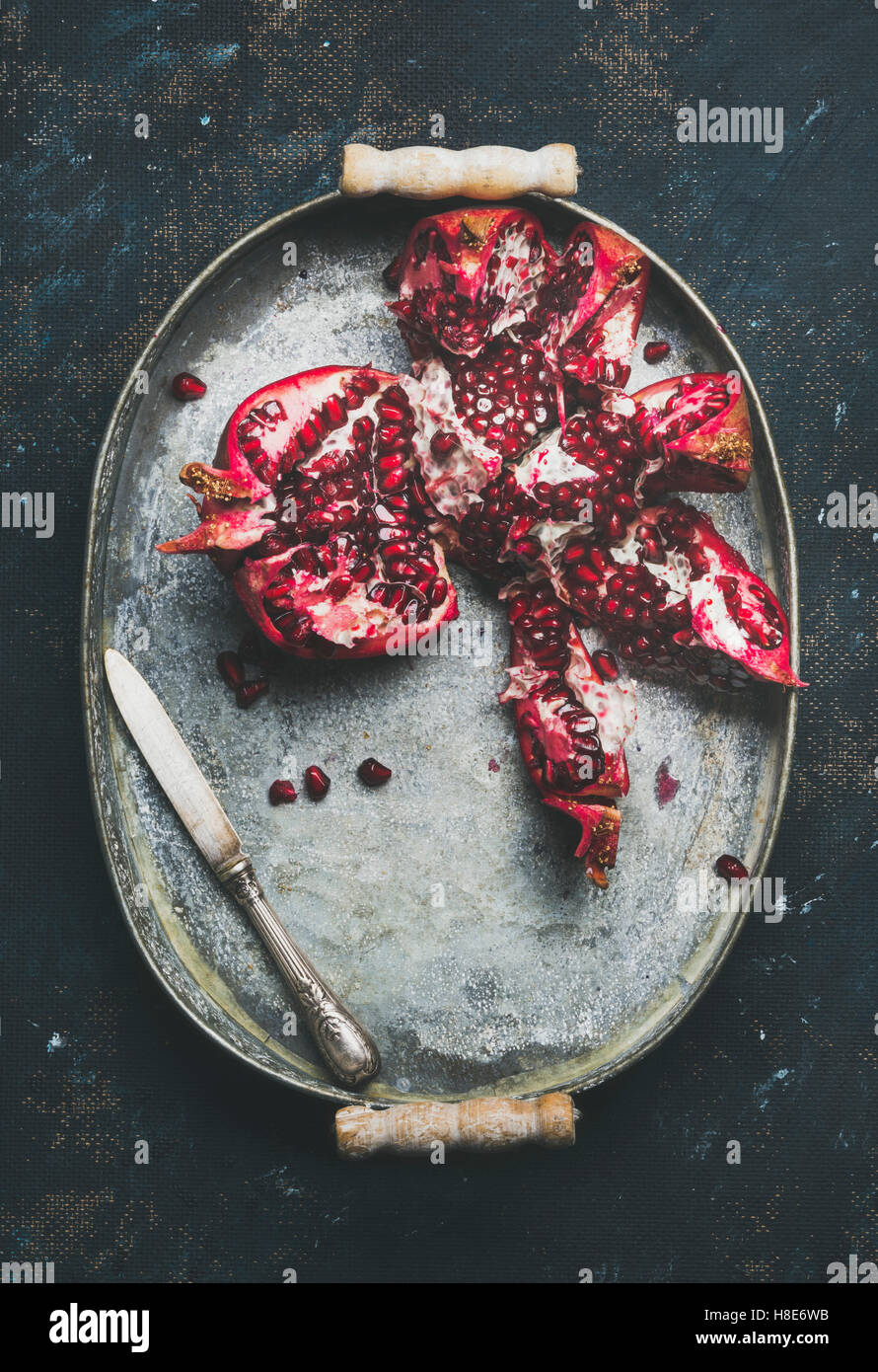 Fresh ripe pomegranate broken in pieces in vintage metal tray over dark blue plywood background, top view, copy space, vertical Stock Photo