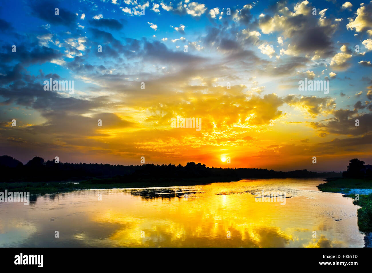 Beautiful lake landscape with vivid sunrise on the cloudy sky. River landscape. Beautiful summer landscape with golden sunset. Stock Photo
