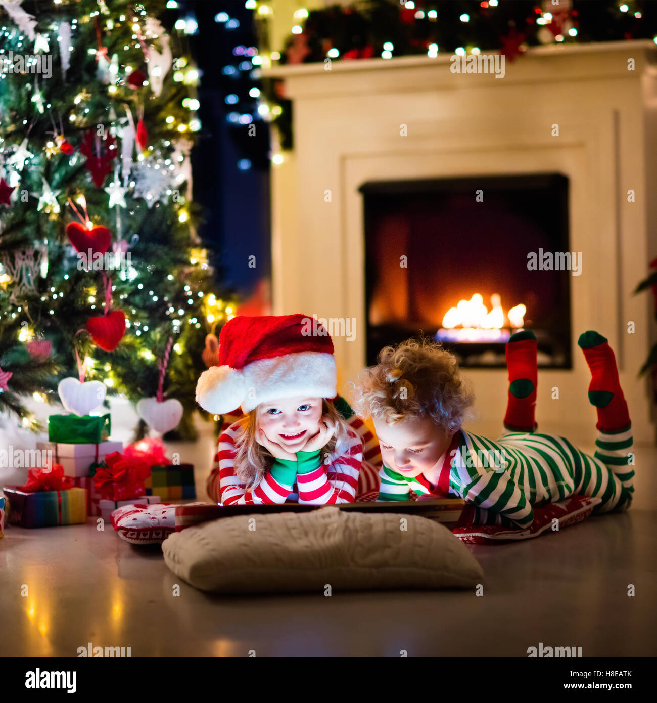 Family on Christmas eve at fireplace. Kids opening Xmas presents. Children under Christmas tree with gift boxes. Stock Photo