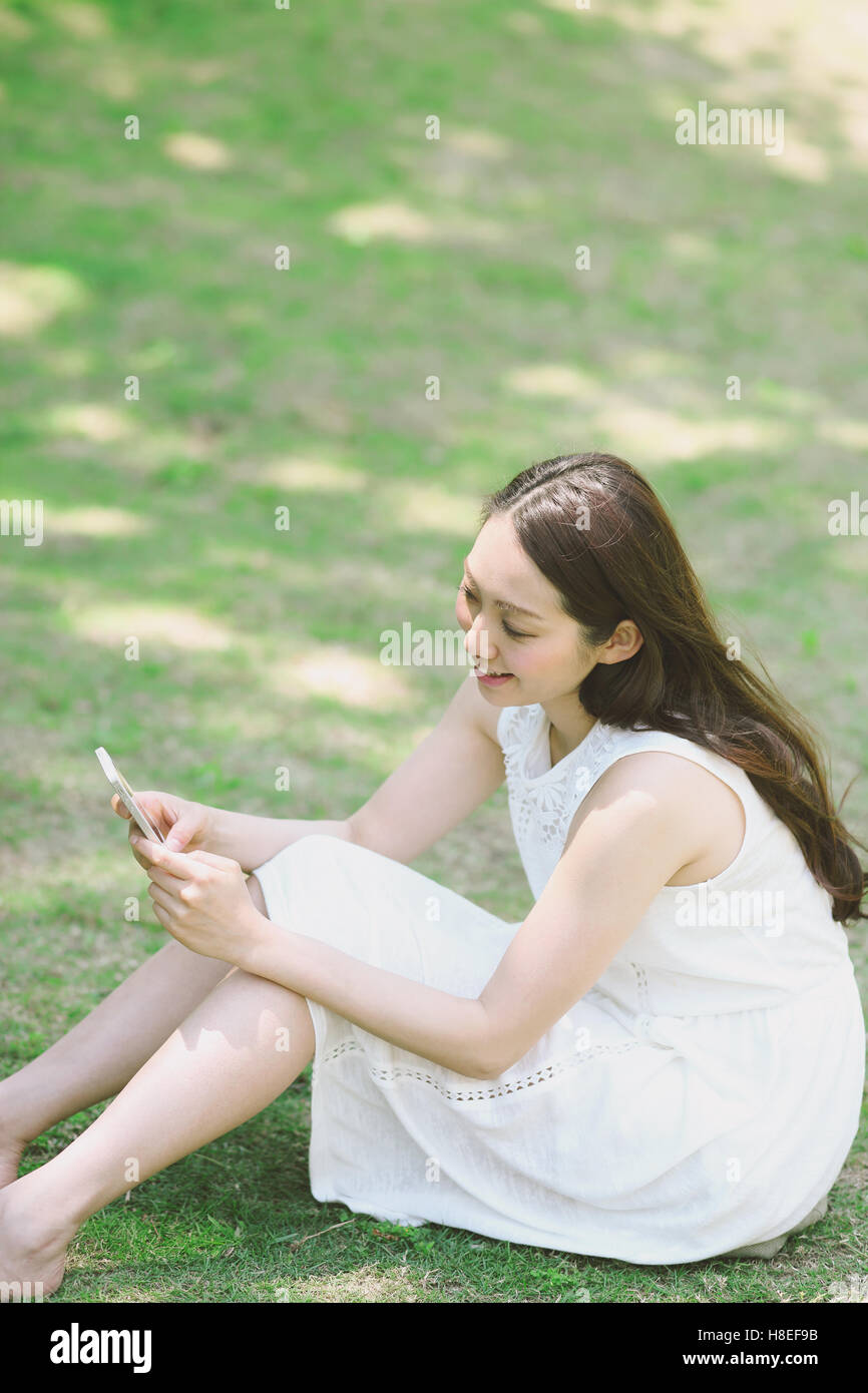 Portrait of young Japanese woman laying on grass with smartphone Stock Photo