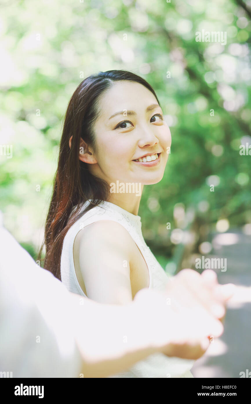 Young Japanese woman holding man's hand and smiling in a city park Stock Photo