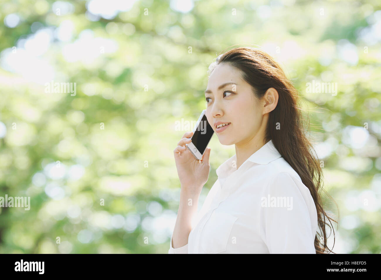 Young Japanese woman on the phone surrounded by green in a city park Stock Photo
