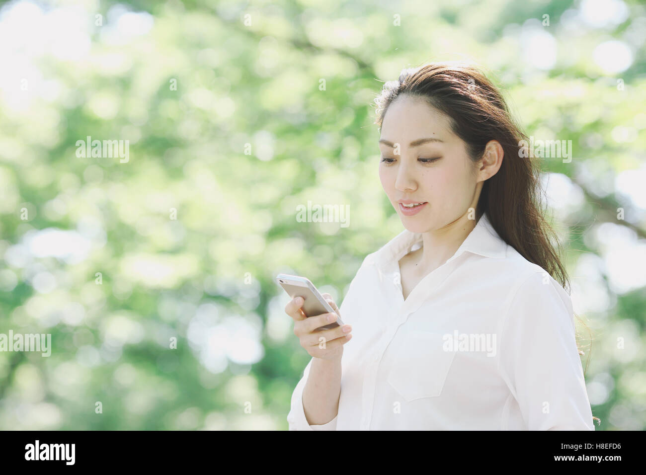 Young Japanese woman with smartphone surrounded by green in a city park Stock Photo