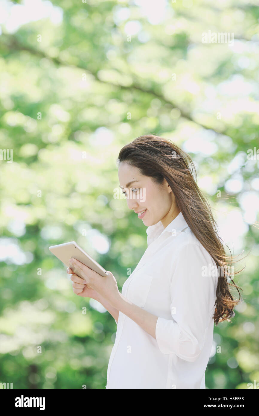 Young Japanese woman with tablet surrounded by green in a city park Stock Photo