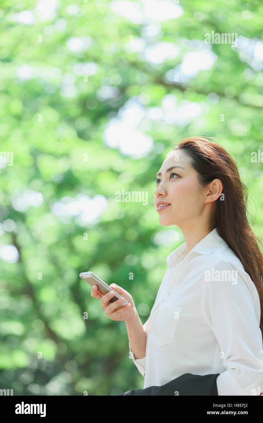 Young Japanese woman with smartphone surrounded by green in a city park Stock Photo
