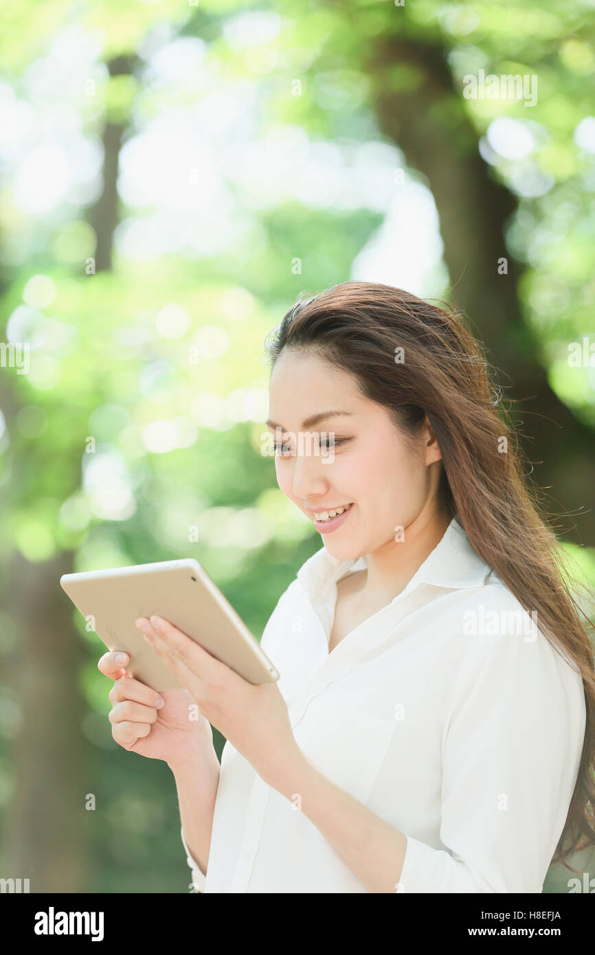 Young Japanese woman with tablet surrounded by green in a city park Stock Photo