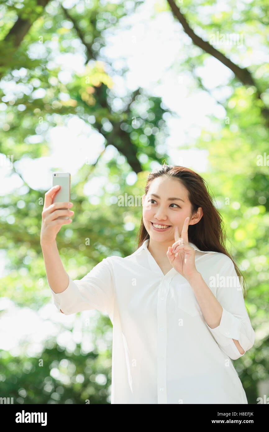 Young Japanese woman taking selfie surrounded by green in a city park Stock Photo