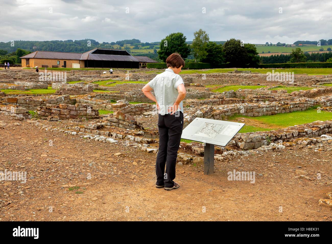 Woman tourist reading information sign. Coria, Corbridge Roman Town and Fort ruins. Corbridge, Northumberland, England, UK. Stock Photo