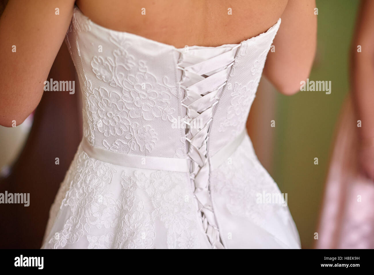 the bride is dressed in a white gown stands back Stock Photo
