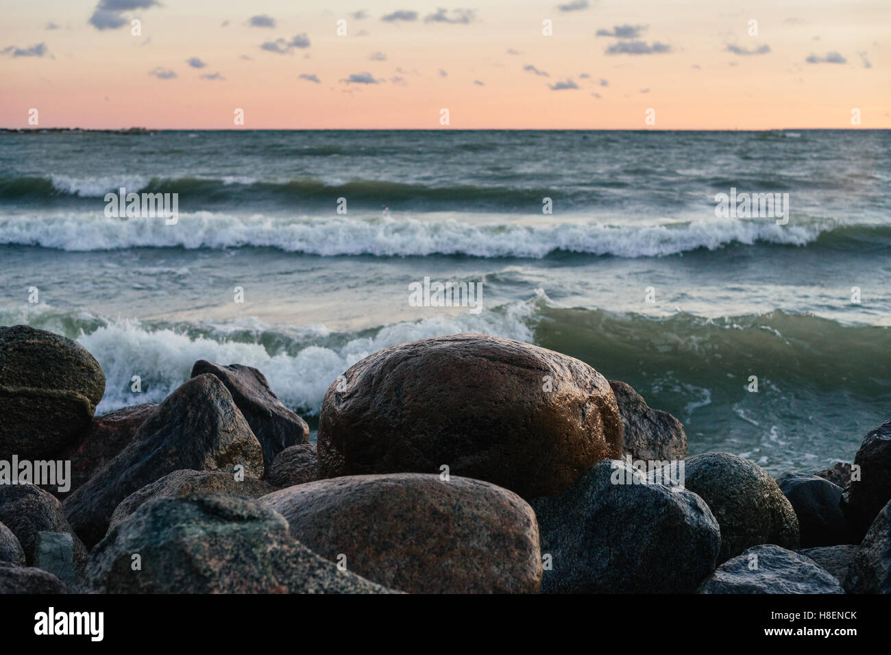 Wet stones against sea waves and sunrise sky. Selective focus on foreground Stock Photo