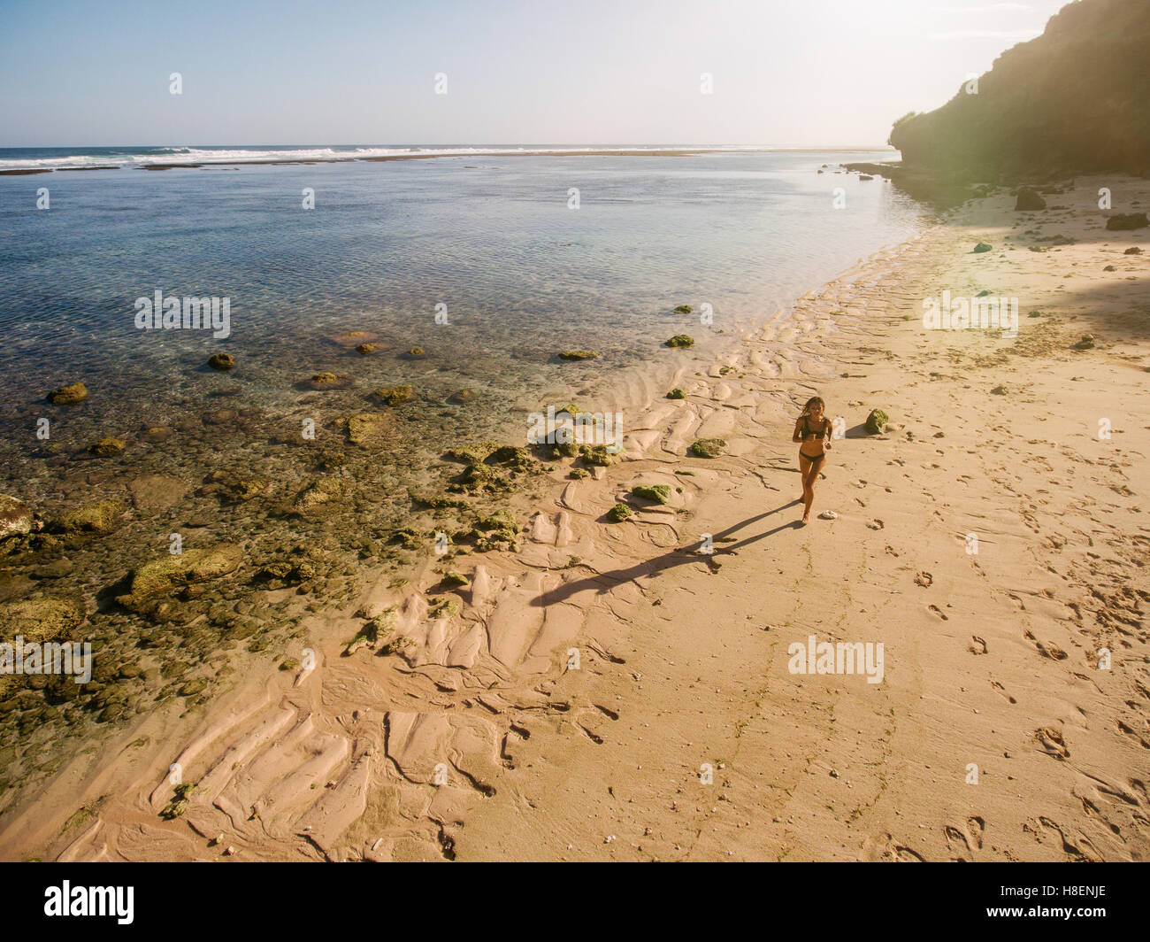 Aerial view of tropical beach with a woman running. Female in bikini