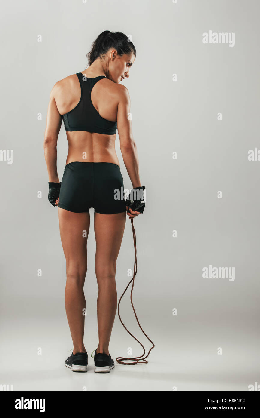 Fit healthy young athlete with a skipping rope standing in black sportswear with her back to the camera looking to the side Stock Photo