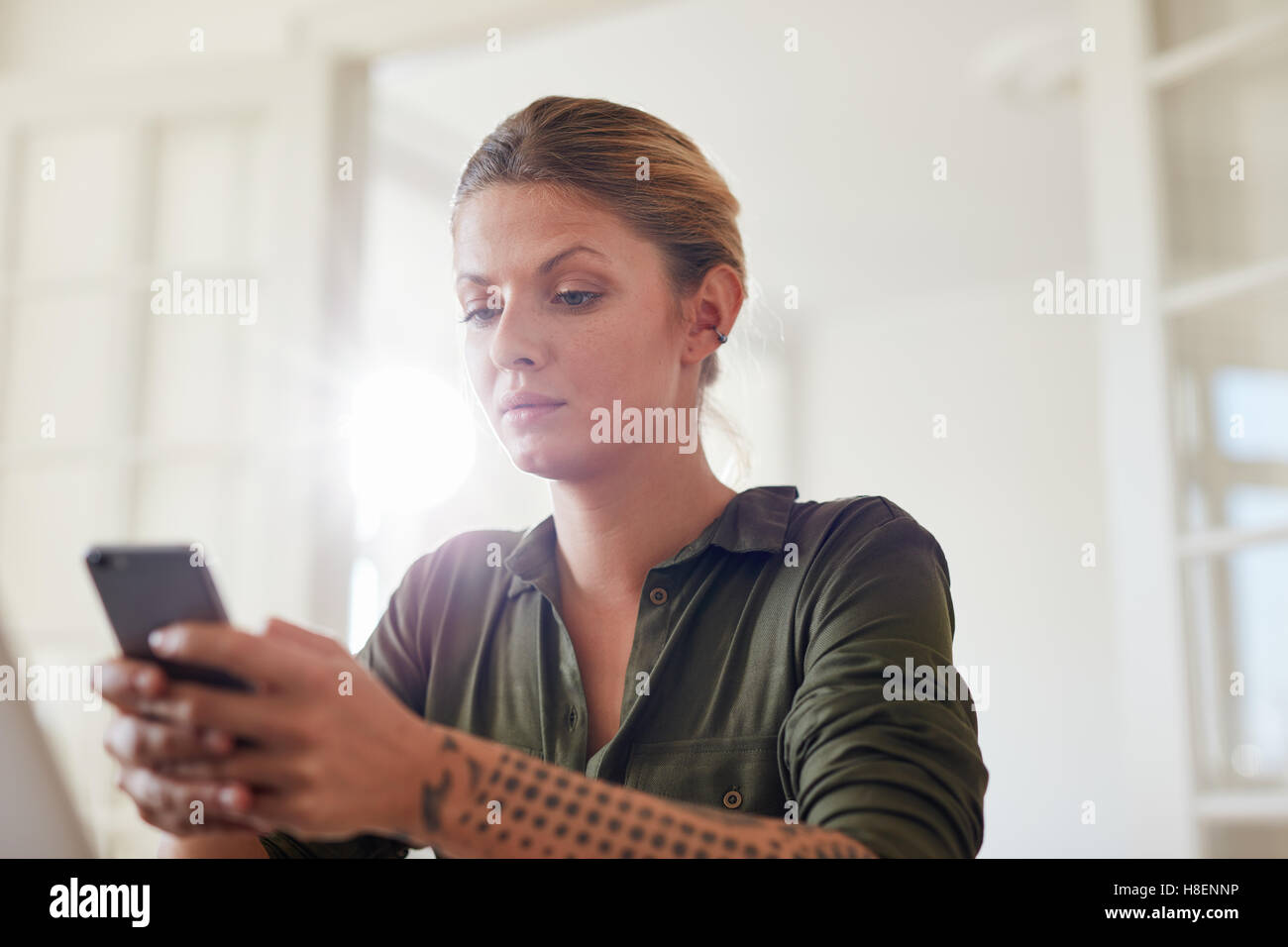 Shot of young woman reading text message on her smart phone while sitting at home. Beautiful caucasian woman using mobile phone. Stock Photo