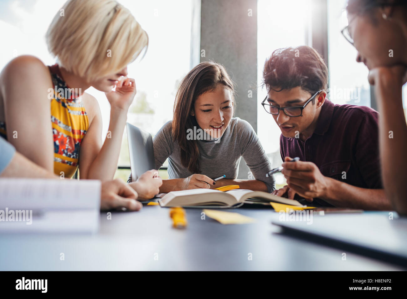 Group of young students working on school assignment in library. Multiethnic young people sitting at table reading reference boo Stock Photo