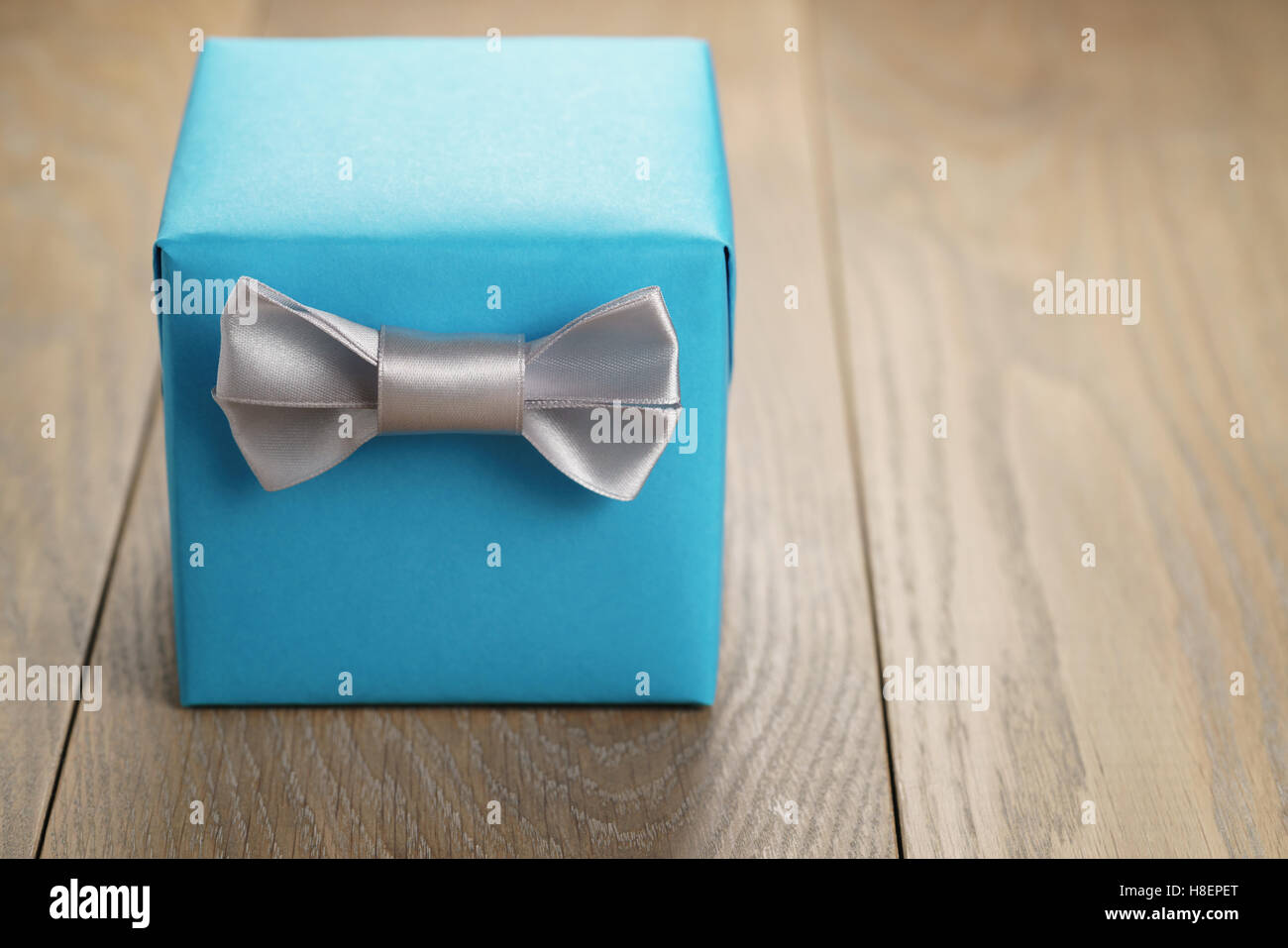 light blue gift box with minimalistic silver ribbon bow on wooden table Stock Photo