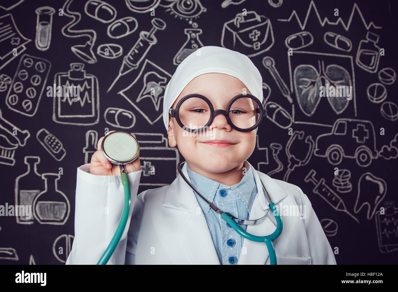 Happy little boy in doctor costume holding sthetoscope on dark