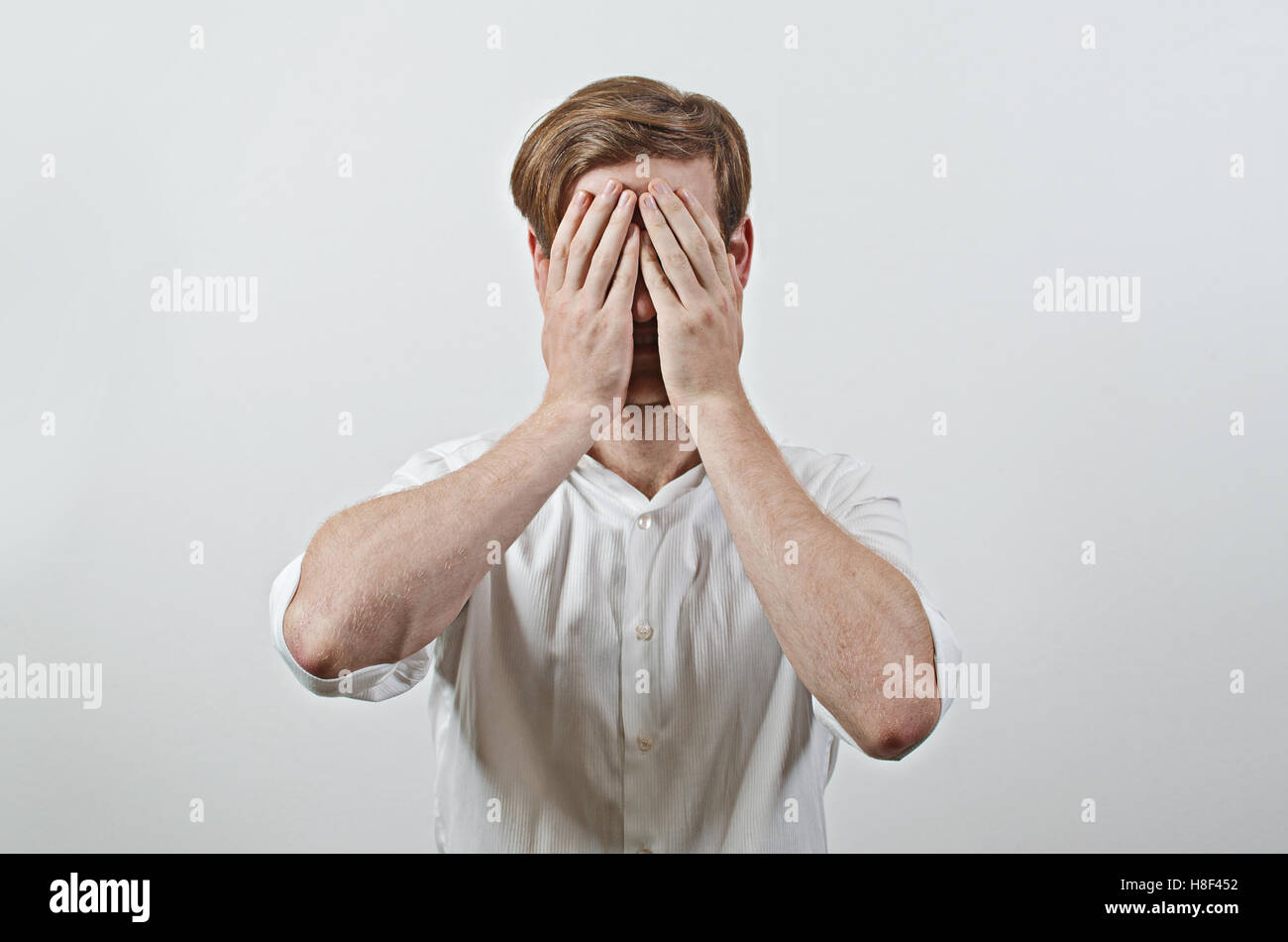 Young Adult Male Wearing White Shirt Covers His Face by Both Hands, Gesturing He Has Made a Big Mistake Stock Photo