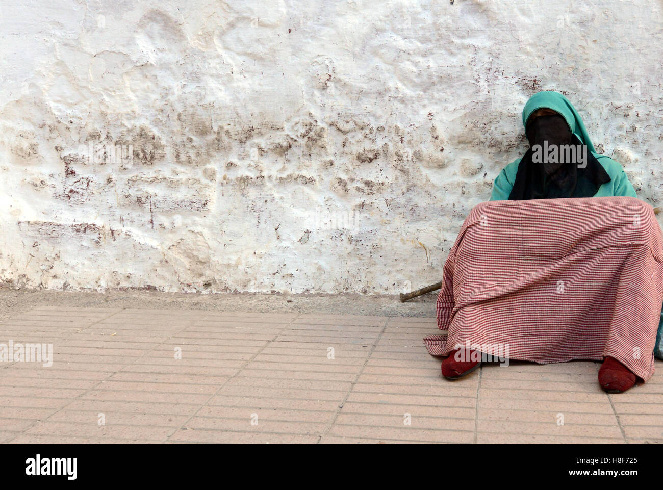 A veiled woman sitting by a colorful wall in the old city of Sale near Rabat, Morocco. Stock Photo