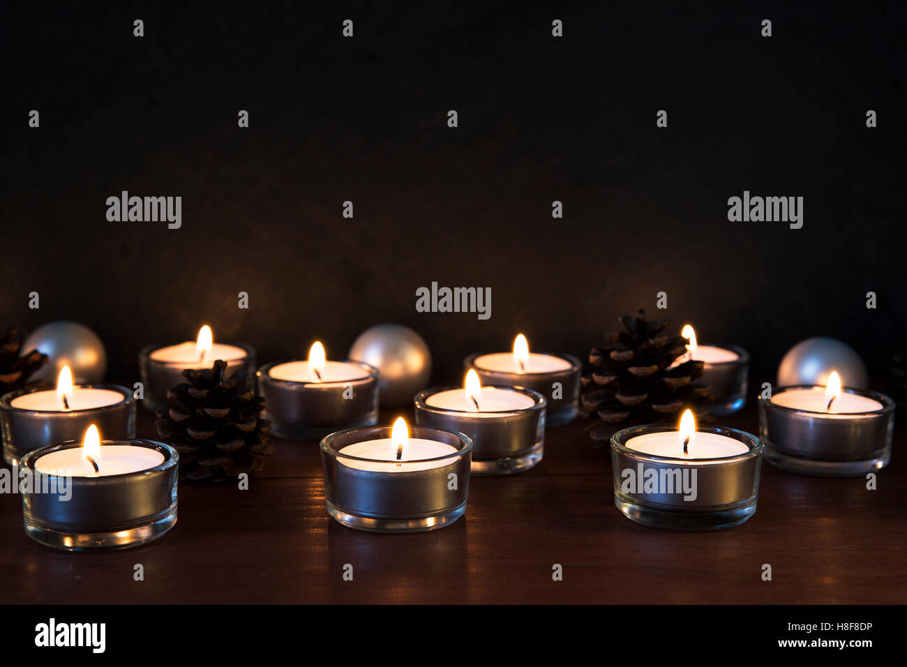 Tea lights with pine cones and baubles on a wooden surface, with copy space. Stock Photo