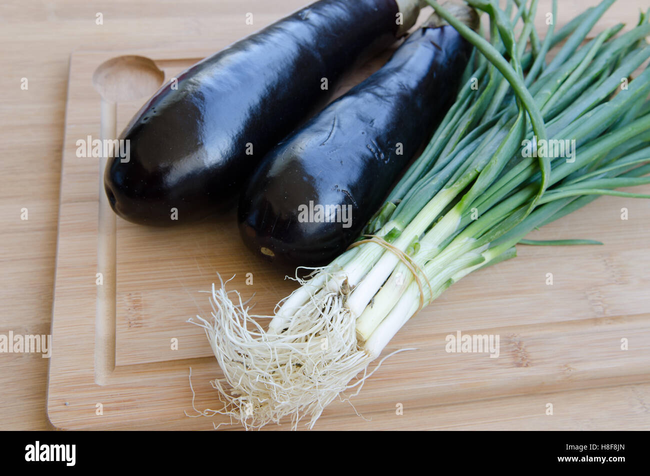 Eggplant with green onions on cutting board Stock Photo