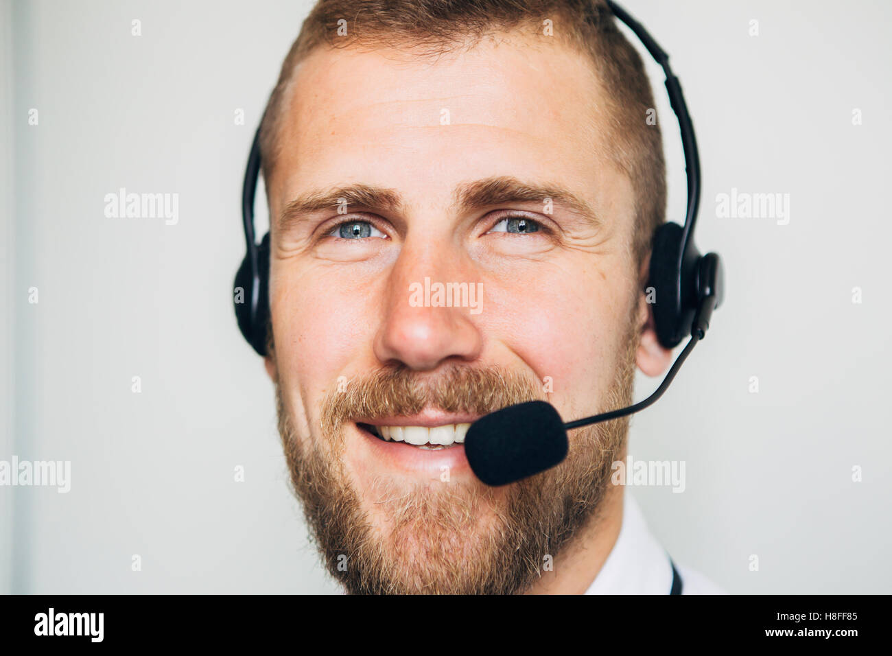 Portrait of handsome young male operator in headset looking at camera and smiling while standing against white background Stock Photo