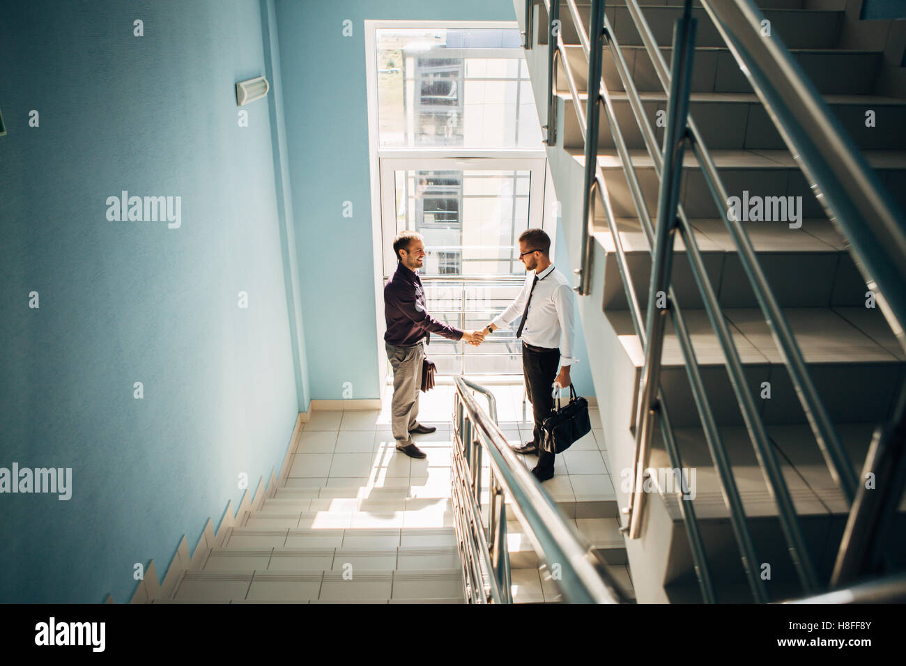 Full length side view of businessmen shaking hands in office building ...