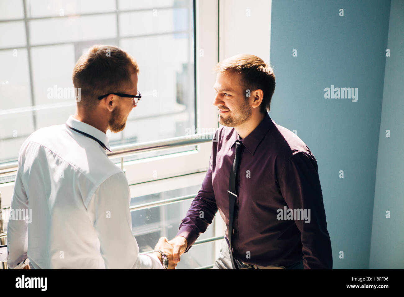 Full length side view of businessmen shaking hands in office building ...