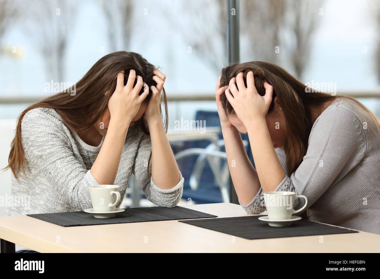Two desperate sad girls crying with hands over head in a bar with a window with a winter background Stock Photo