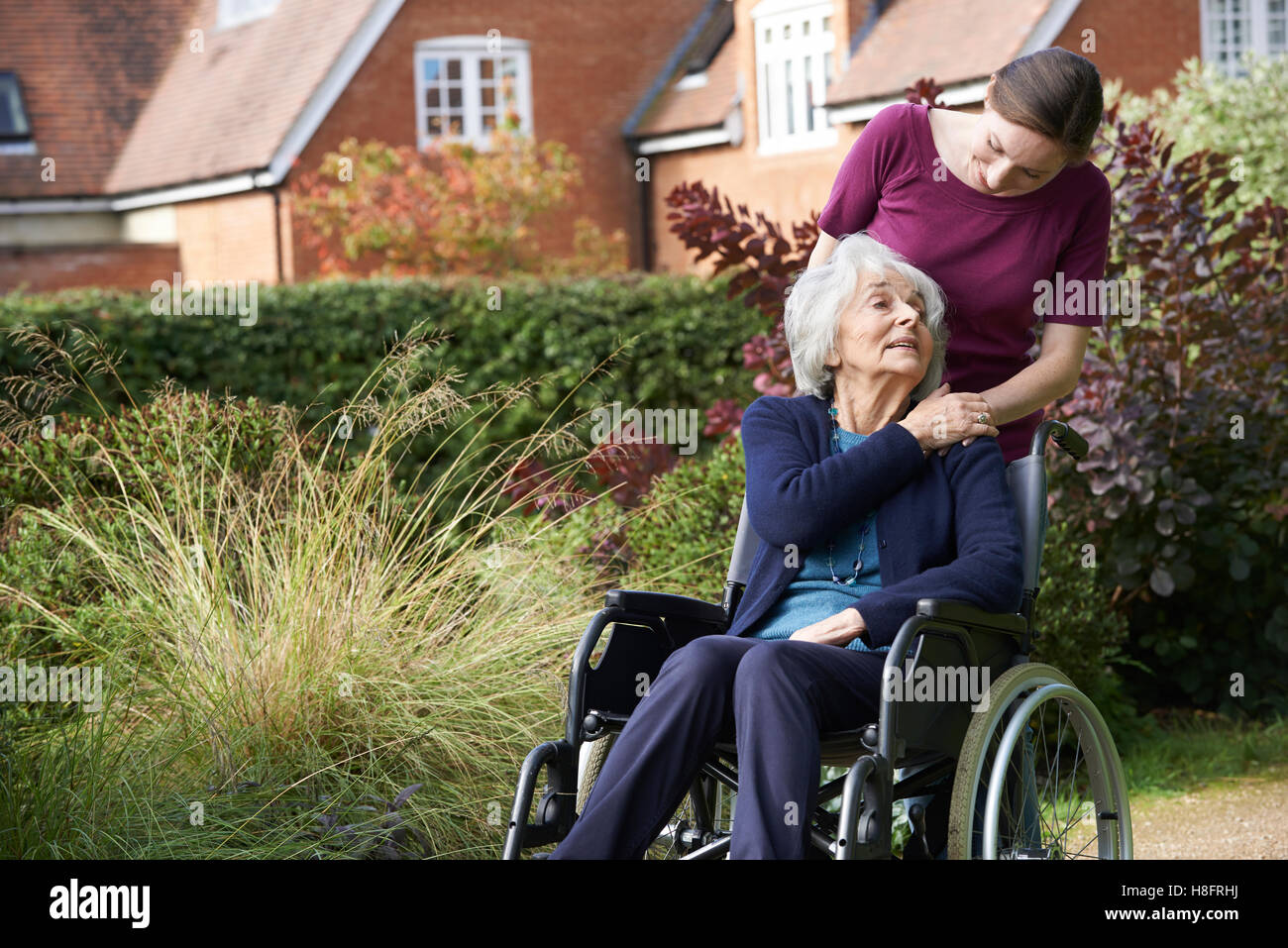 Daughter Pushing Senior Mother In Wheelchair Stock Photo