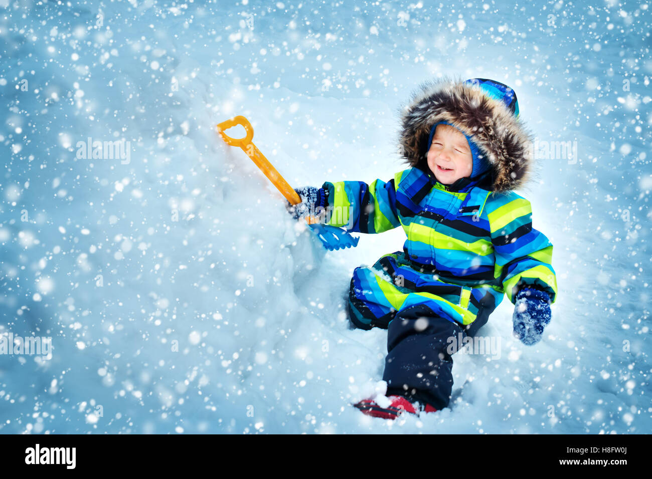 Boy in knitted hat, gloves and scarf outdoors at snowfall Stock Photo
