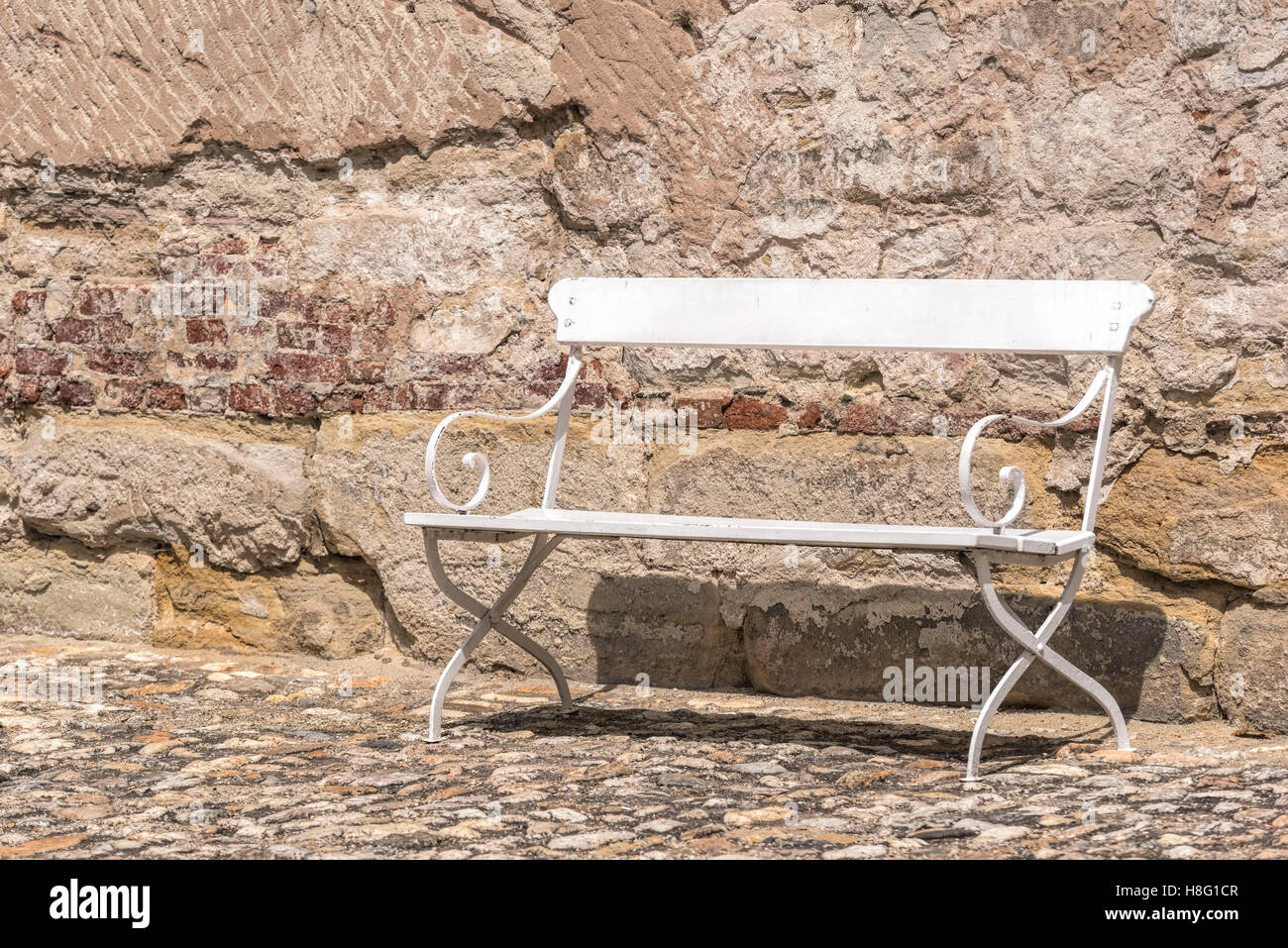 Old white bench on cobblestones in front of a wall Stock Photo - Alamy