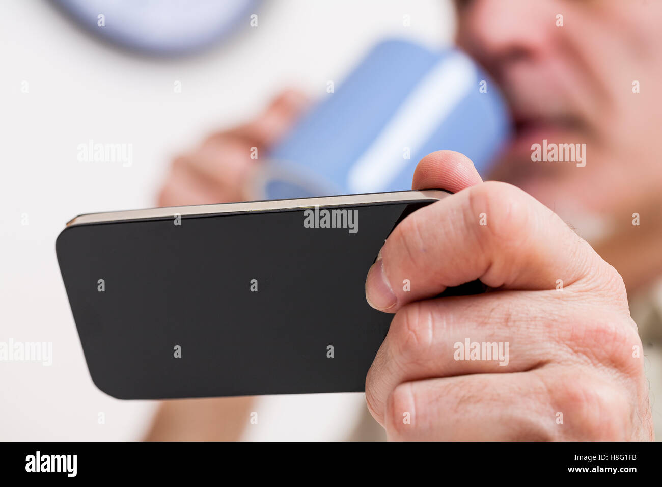 focus on a generic mobile phone held by a mature man blurred on the background in his kitchen Stock Photo