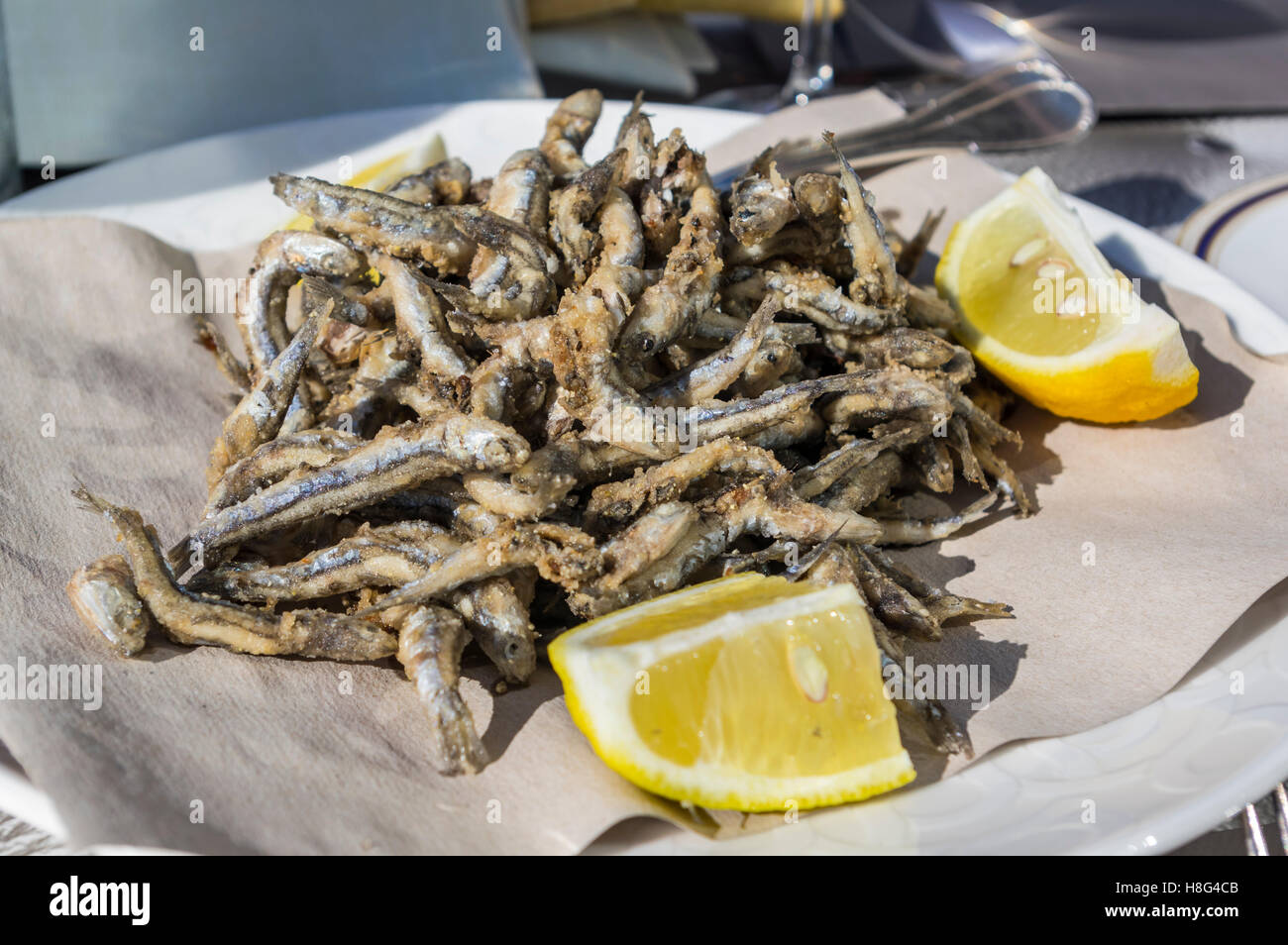 Plate of small European anchovies (engraulis encrasicolus), deep-fried as whole fishes and served with lemon. Typical dish of Liguria, Italy. Stock Photo