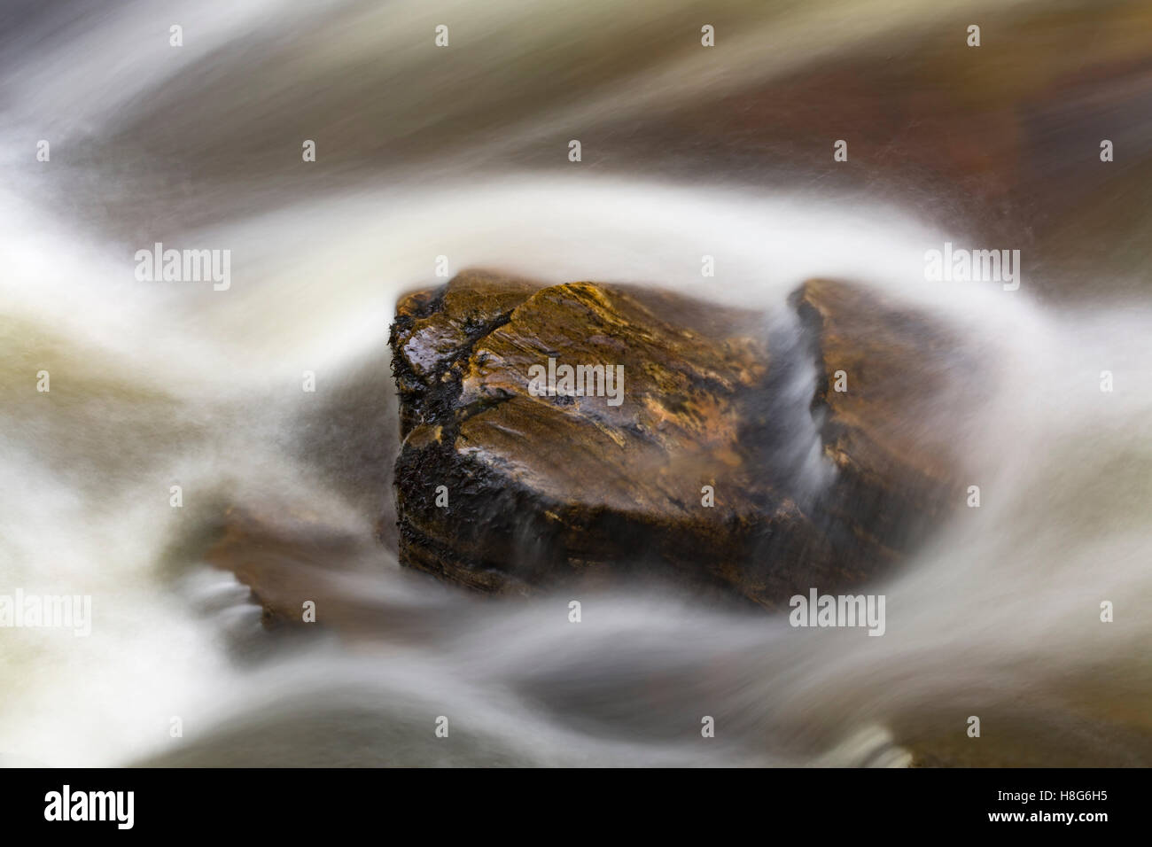 Blurred water flowing over a small rock. Stock Photo