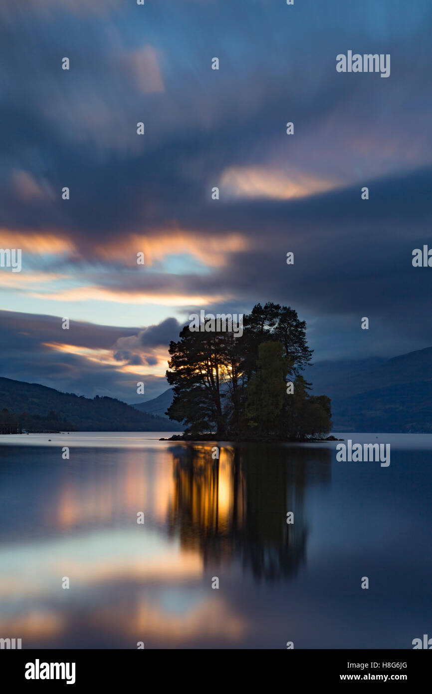Loch Tay, Perthshire, Scotland, reflects the light from the setting sun as it passes behind the trees on one of the islands. Stock Photo