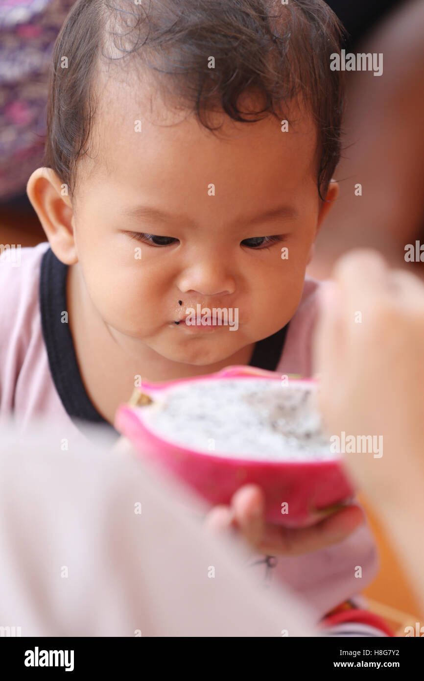 Asian baby eating a dragon fruit with happily,concept of health and foods of the children. Stock Photo