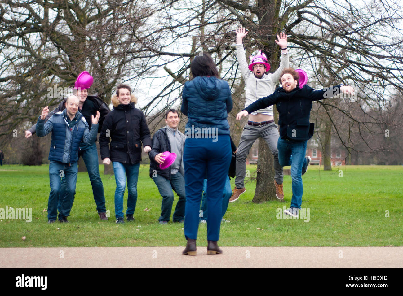 London: Group of men looking at a lady's camera and involving her at Hyde Park. They came from France for a Stag Night. Stock Photo