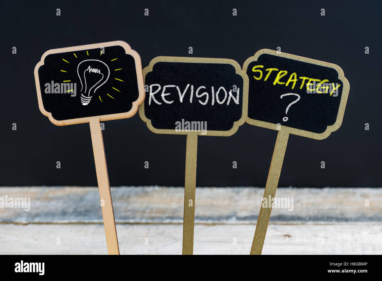 Concept message REVISION STRATEGY ? and light bulb as symbol for idea written with chalk on wooden mini blackboard labels Stock Photo