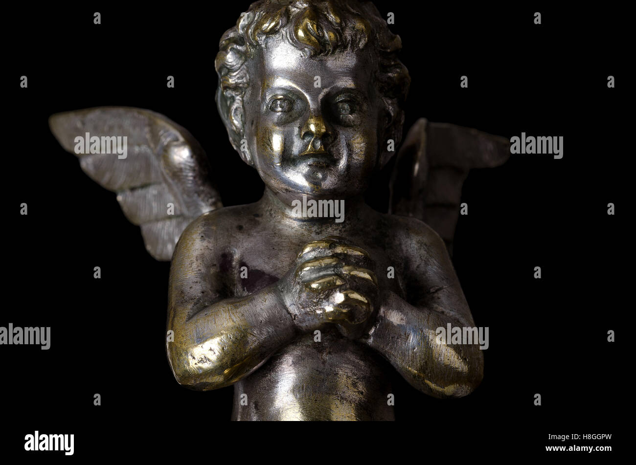 Praying winged putto on black background. Angel made of brass, covered with silver, as part of a candelabra. Stock Photo