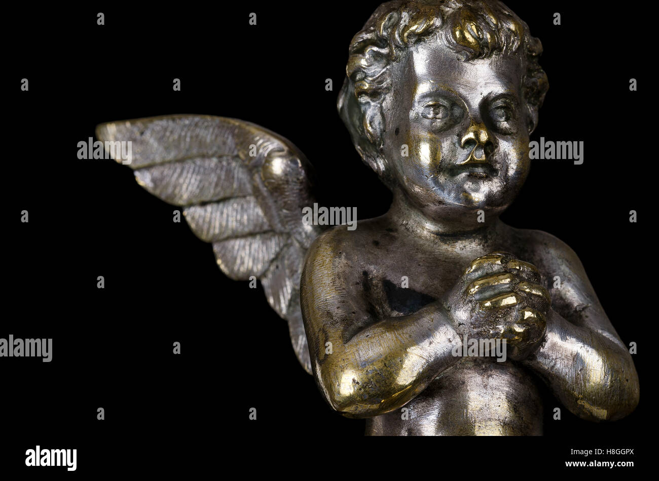 Praying winged putto side view on black background. Angel made of brass, covered with silver, part of a candelabra. Stock Photo