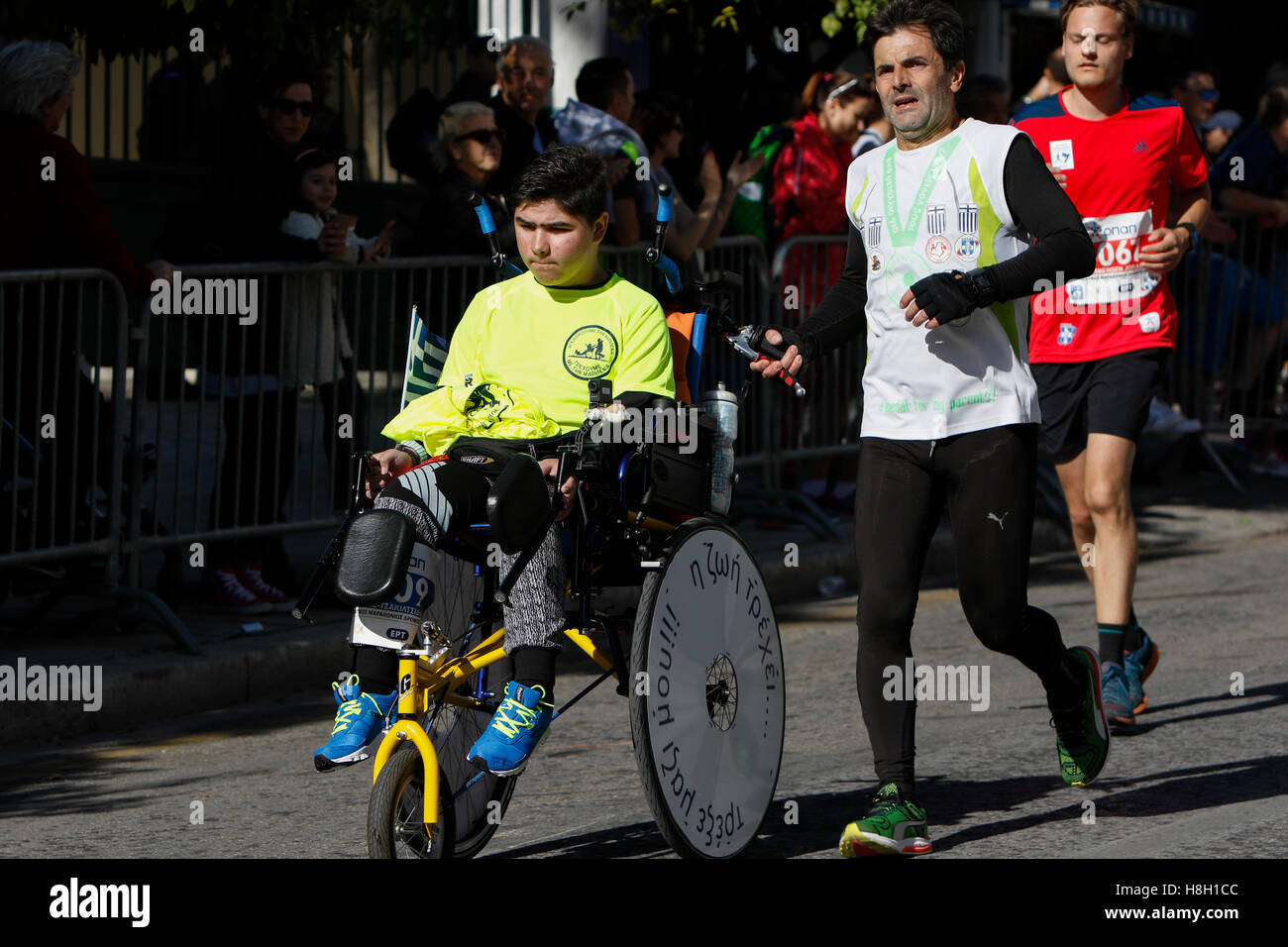 Athens, Greece. 13th November 2016. A runner pushes a boy in a wheel chair. Thousands of people from all over the world took part in the 2016 Athens Marathon the Authentic, which starts in the town of Marathon and is ending in Athens, the route, which according to legend was first run by the Greek messenger Pheidippides in 490 BC. Stock Photo
