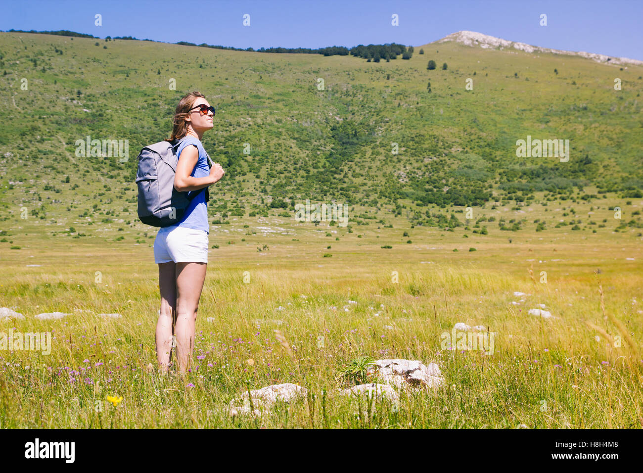 Young woman backpacker standing in green meadow in unspoiled nature Stock Photo