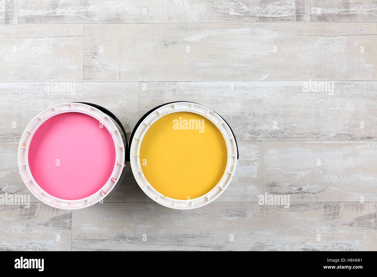 Looking down on two open paint cans of coloured paint  stood on a shabby style wood floor Stock Photo