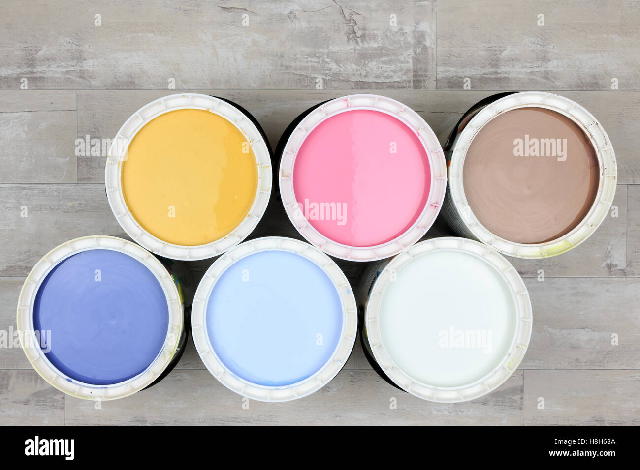 Looking down on six open paint cans of coloured paint  stood on a shabby style wood floor Stock Photo