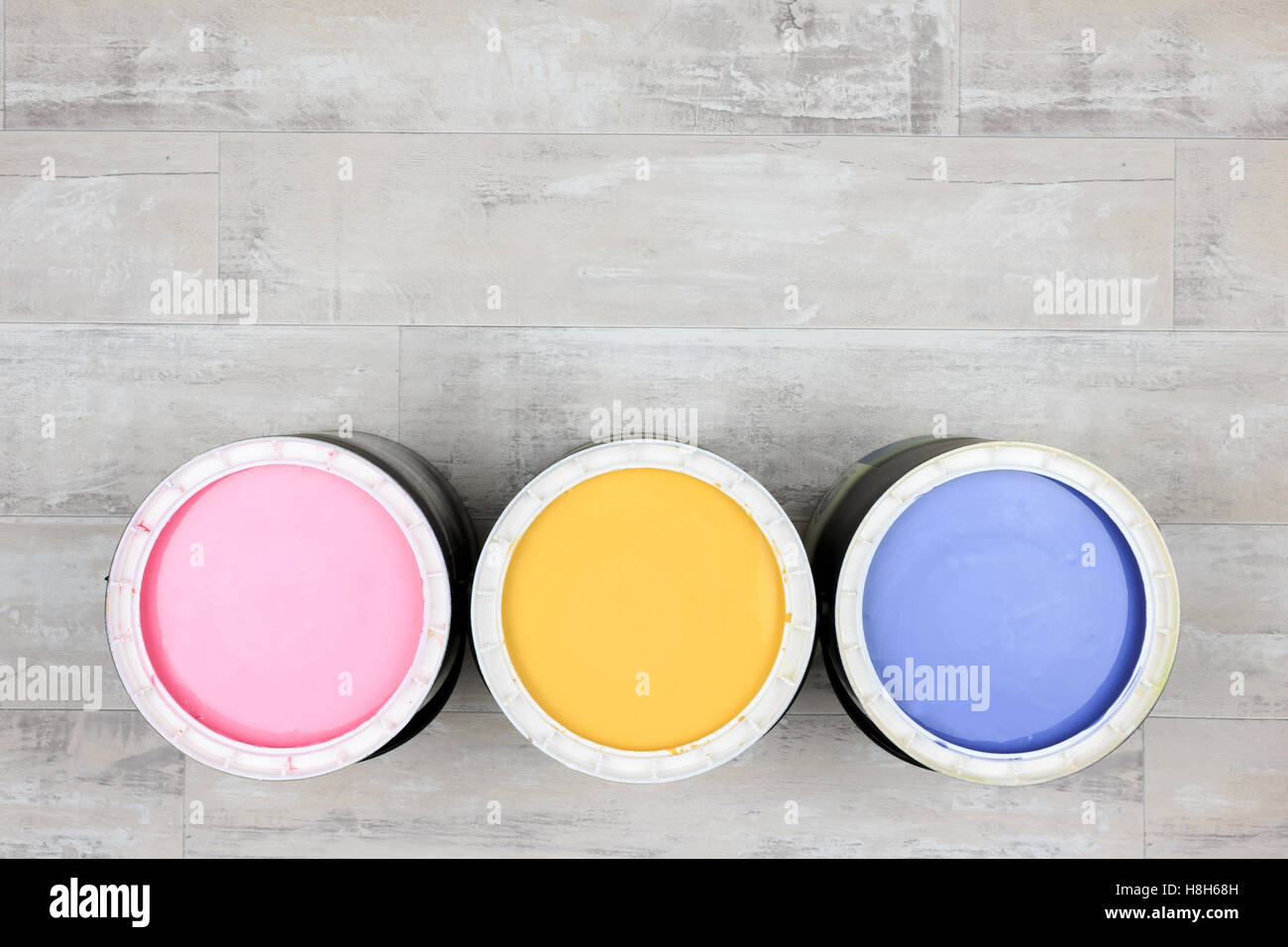 Looking down on three open paint cans of coloured paint stood on a shabby style wood floor Stock Photo