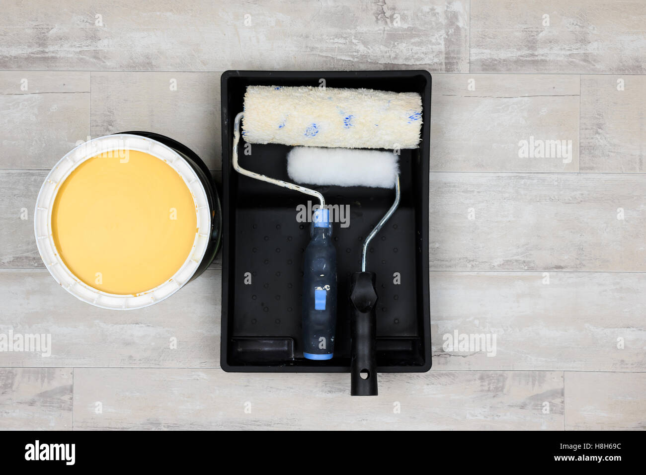 Looking down on an open paint can of yellow paint with paint tray and paint rollers on a shabby style wood floor Stock Photo